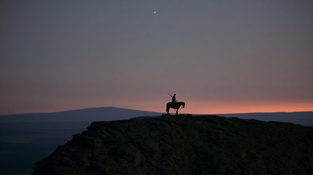 A lone rider on a ridge under a wide dawn sky.