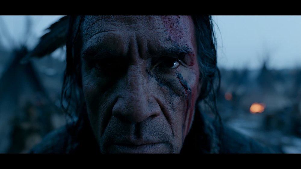 An elder's face lit by fire on the night plains.